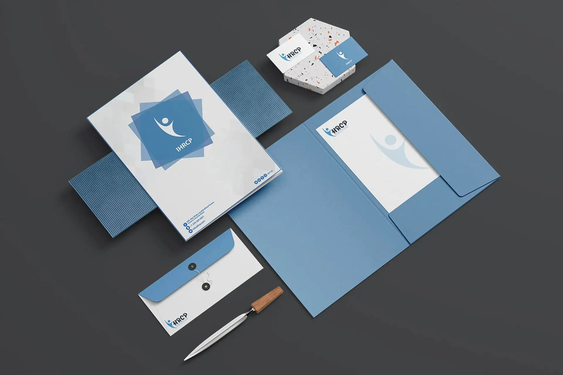IHRCP Organization Stationery Branding Mockup: A sophisticated, coordinated set of corporate branding materials for a non-profit organization (IHRCP), including a folder, envelope, business cards, and a notebook. The design uses a clean white and light blue color palette, featuring a logo that symbolizes a person with open arms or embracing a concept, suitable for human rights, aid, or social care organizations.
