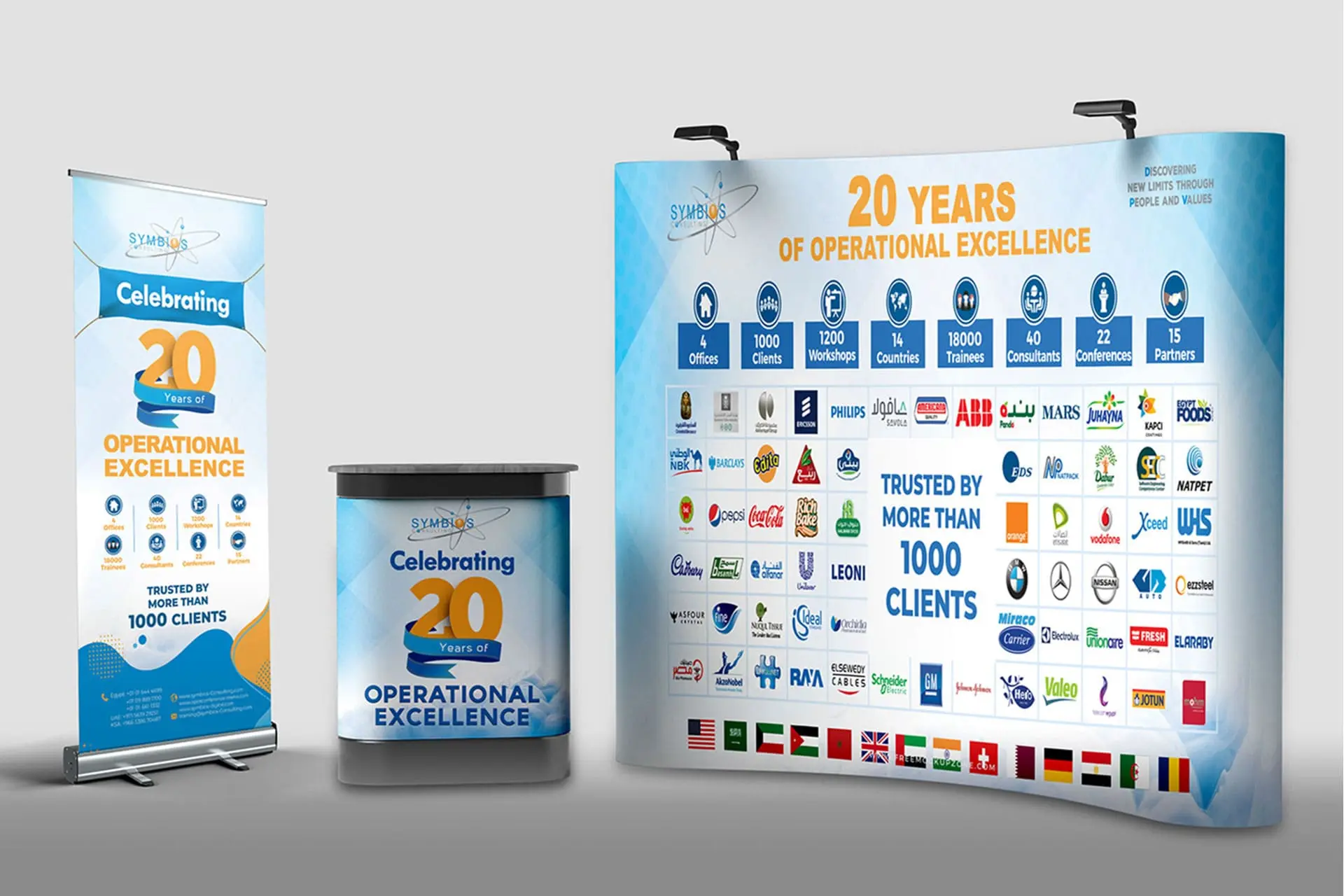 Symbios 20 Years of Operational Excellence Exhibition Stand: A large trade show booth design promoting Symbios's 20th anniversary, showcasing key metrics (1000+ clients, 1200 workshops, 40 consultants) and a collage of over 100 client logos, emphasizing business consulting and operational excellence achievements. B2B services and corporate event marketing.