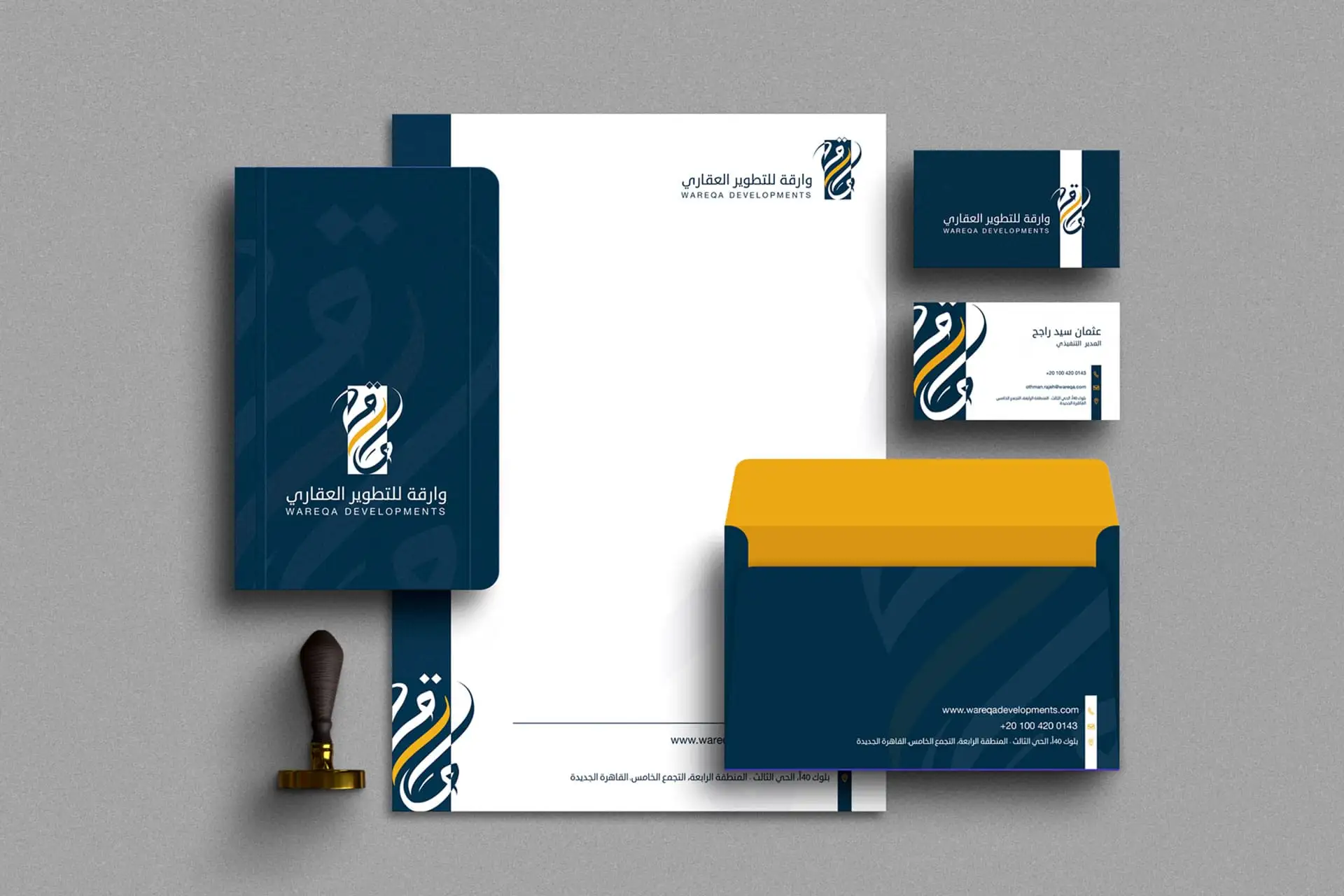 Wareqa Developments Corporate Stationery Mockup: A professional set of business materials for a real estate development company, featuring a dark blue/navy and gold/yellow color palette. The display includes letterheads, business cards, and an envelope, showcasing the Wareqa logo—a stylized Arabic letter 'Waw' combined with a flame or sword icon. Corporate branding for investment and property firms.